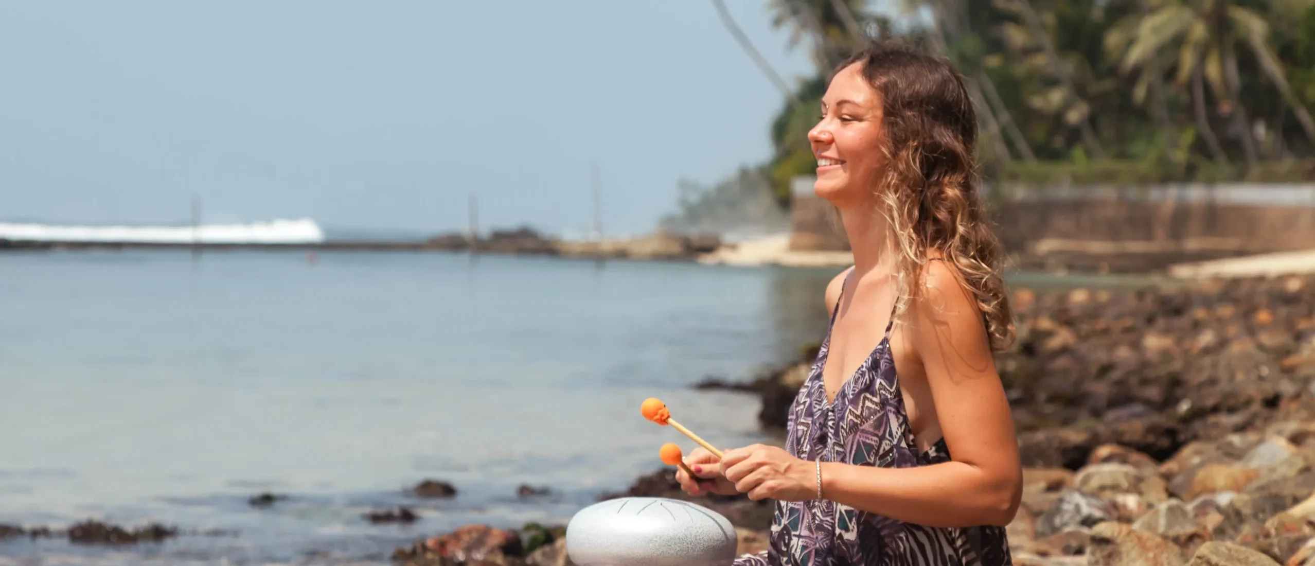 Young woman playing on tank drum on the coast of the azure sea - Experience Healing Through Sound: Join Ciao Bella for a Transformative Gong Immersion in the Florida Keys