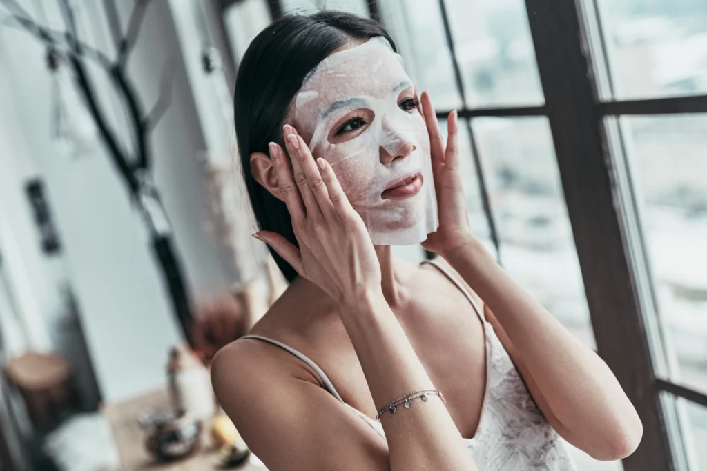 relaxing woman applying facial mask indoors - The Glow Countdown: When to Start Your Bridal Skincare Routine for Flawless Wedding-Day Skin - Ciao Bella Salon Spa Islamorada